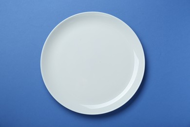 Photo of Empty white ceramic plate on blue background, top view