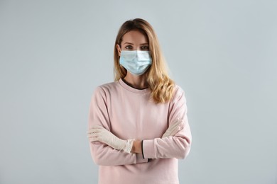 Young woman in medical gloves and protective mask on grey background