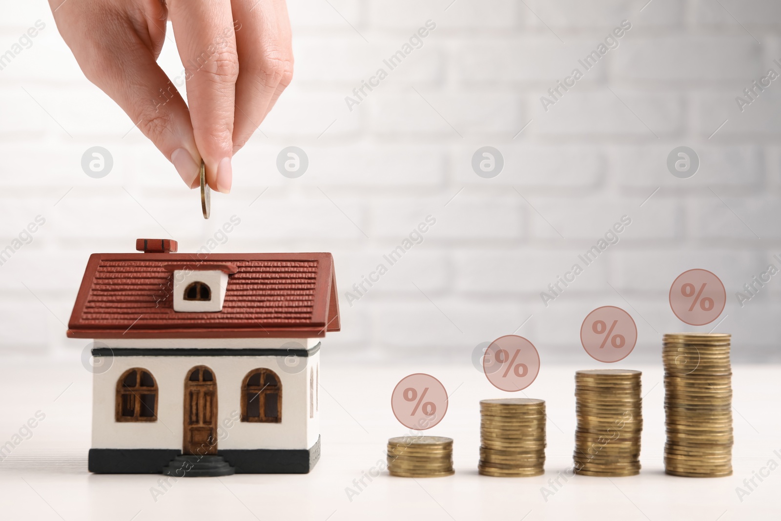 Image of Mortgage rate. Woman putting coin into house shaped money box, closeup. Stacked coins and percent signs