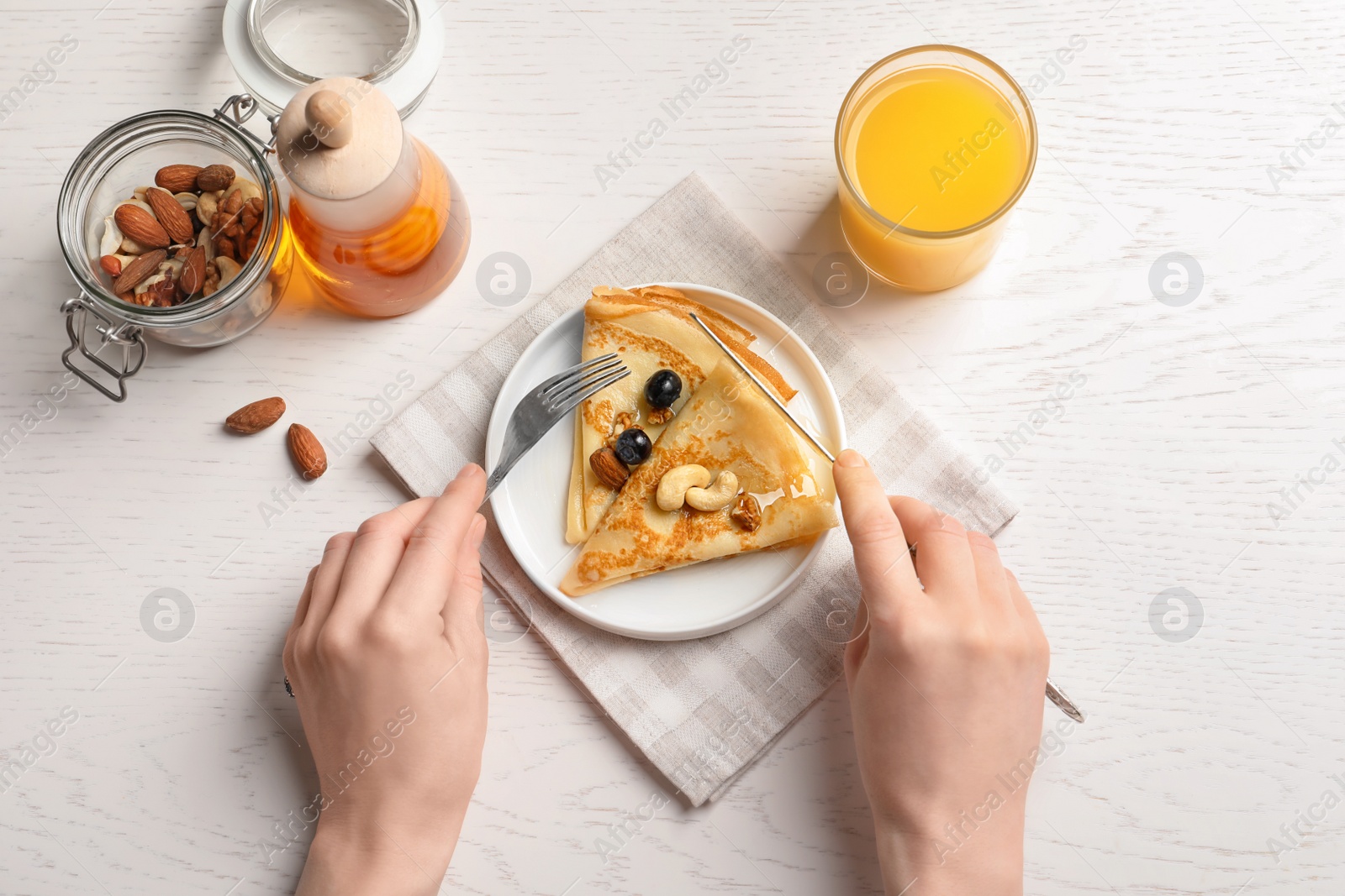 Photo of Woman eating thin pancakes with berries and nuts at table, top view