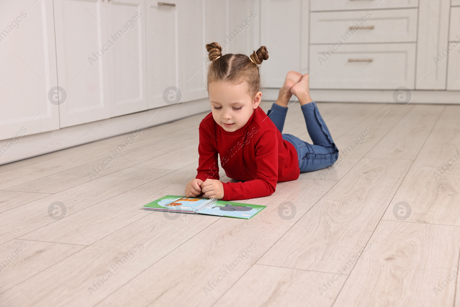 Photo of Cute little girl reading book on warm floor in kitchen, space for text. Heating system