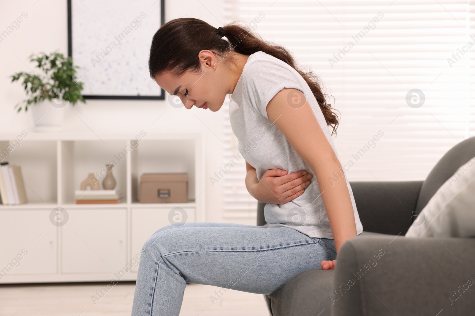 Photo of Woman suffering from abdominal pain on sofa at home. Unhealthy stomach