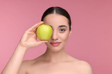 Beautiful young woman with apple on pink background