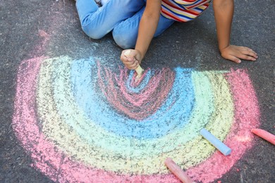 Little child drawing rainbow with colorful chalk on asphalt, closeup