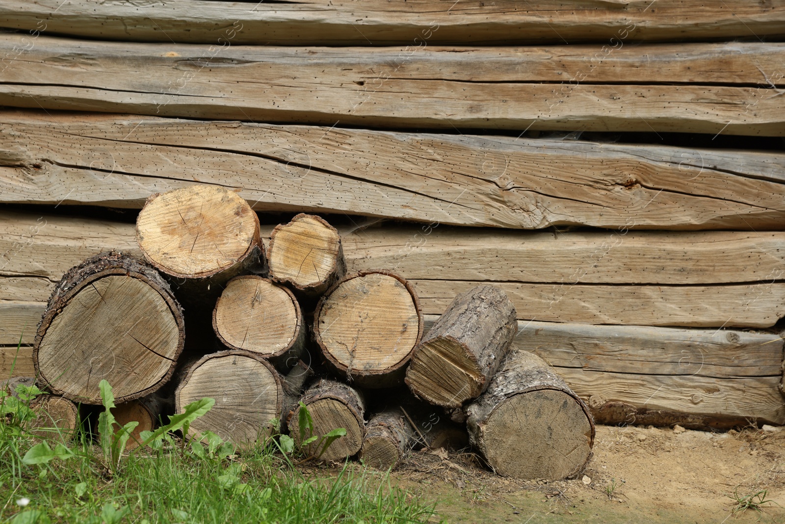 Photo of Pile of cut firewood near wooden wall on summer day, space for text