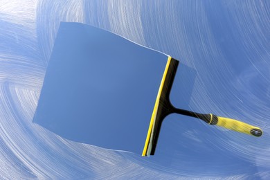 Photo of Squeegee and cleaning foam on glass, closeup