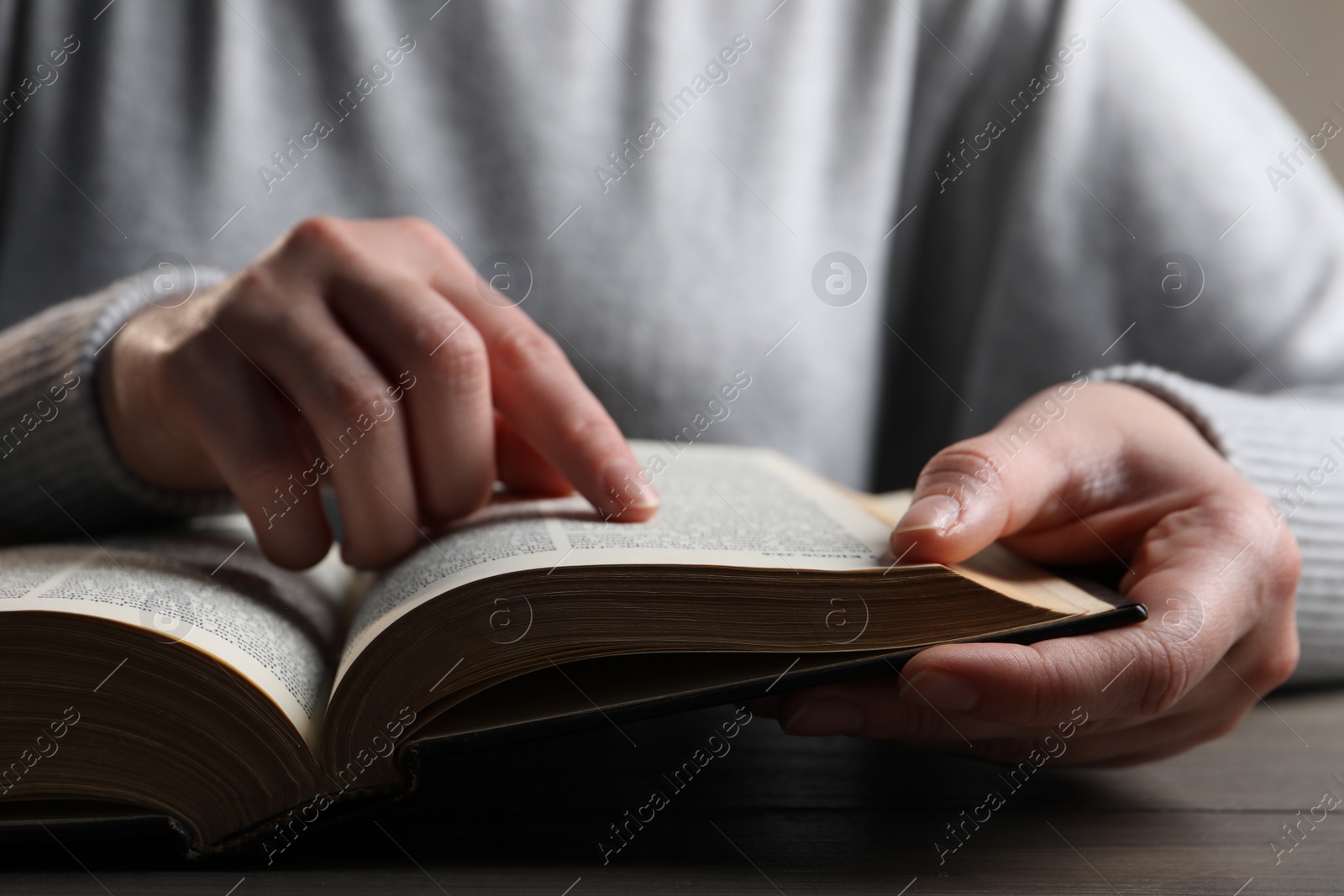 Photo of Woman reading Bible at wooden table, closeup