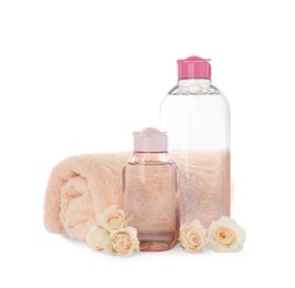 Photo of Bottles of micellar cleansing water, rolled towel and flowers on white background