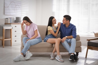 Photo of Unhappy woman feeling jealous while couple spending time together on sofa at home