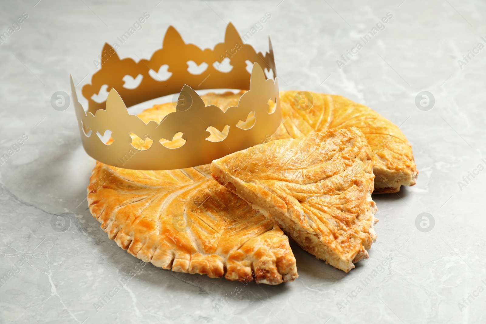 Photo of Traditional galette des Rois with paper crown on light grey marble table