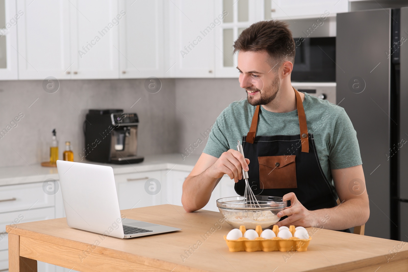 Photo of Happy man learning to cook with online video on laptop at table in kitchen. Time for hobby