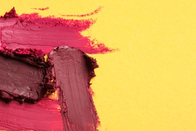 Photo of Smears of bright lipsticks on yellow background, top view. Space for text