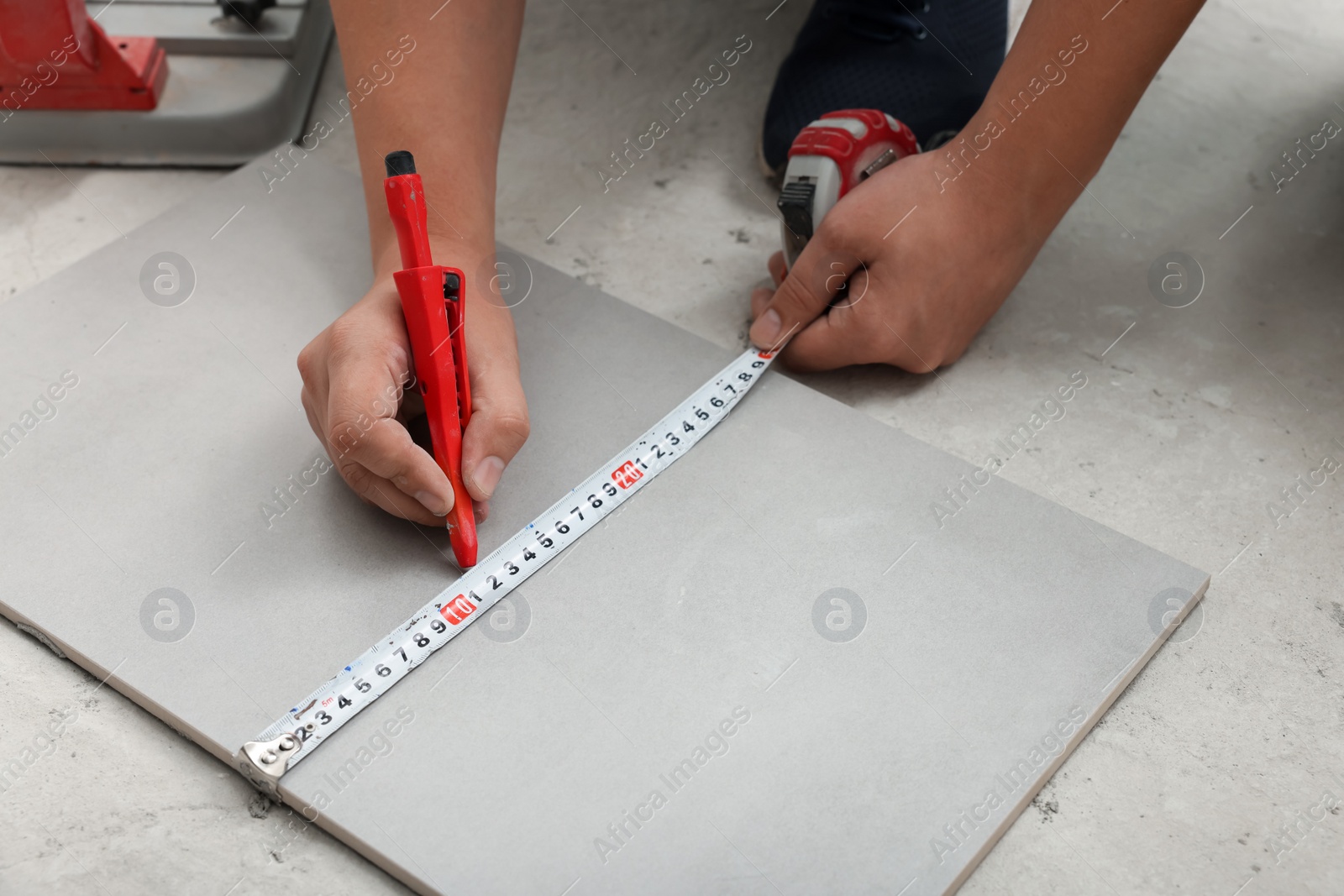 Photo of Worker measuring and marking ceramic tile on floor, closeup