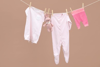 Photo of Different baby clothes and bunny toy drying on laundry line against light brown background