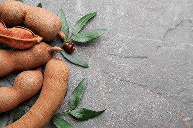 Ripe tamarinds and fresh leaves on grey table, flat lay. Space for text