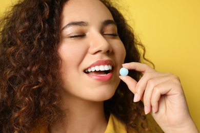 African-American woman taking vitamin pill on yellow background, closeup