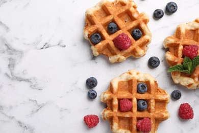 Photo of Delicious Belgian waffles with fresh berries and mint on white marble table, flat lay. Space for text