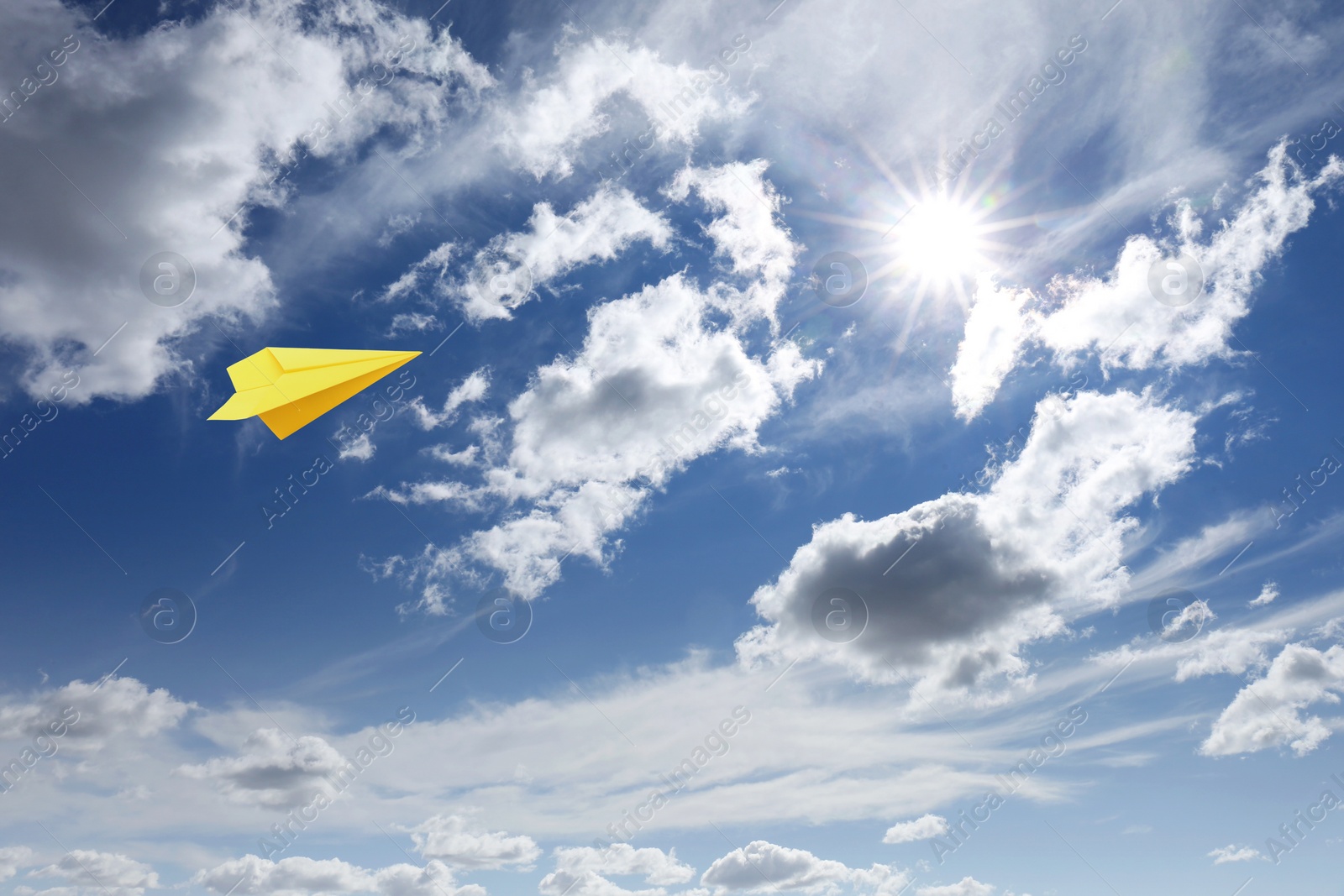 Image of Yellow paper plane flying in blue sky with clouds