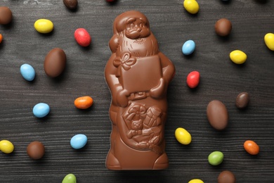 Photo of Flat lay composition of chocolate Santa Claus among sweets on dark grey wooden table