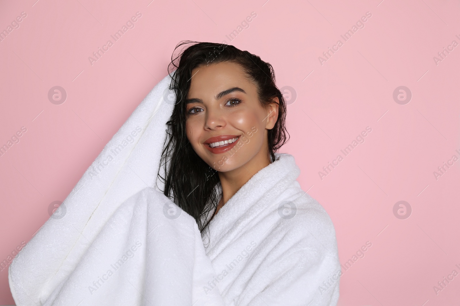 Photo of Beautiful young woman in bathrobe drying hair with towel on pink background