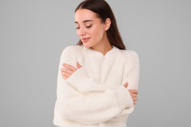 Beautiful young woman in stylish warm sweater on grey background