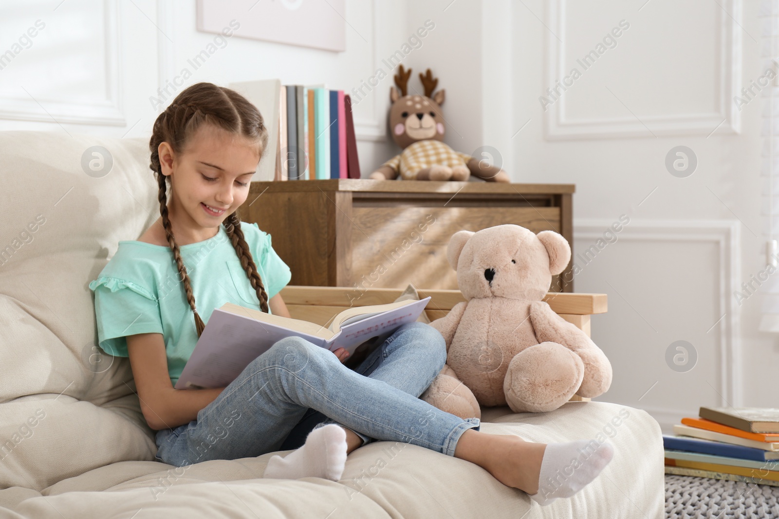 Photo of Cute little girl reading book on sofa at home