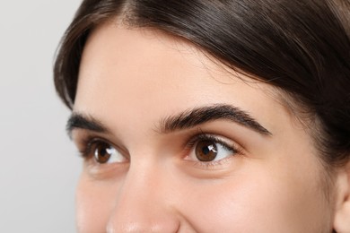 Woman after eyebrow tinting procedure on grey background, closeup