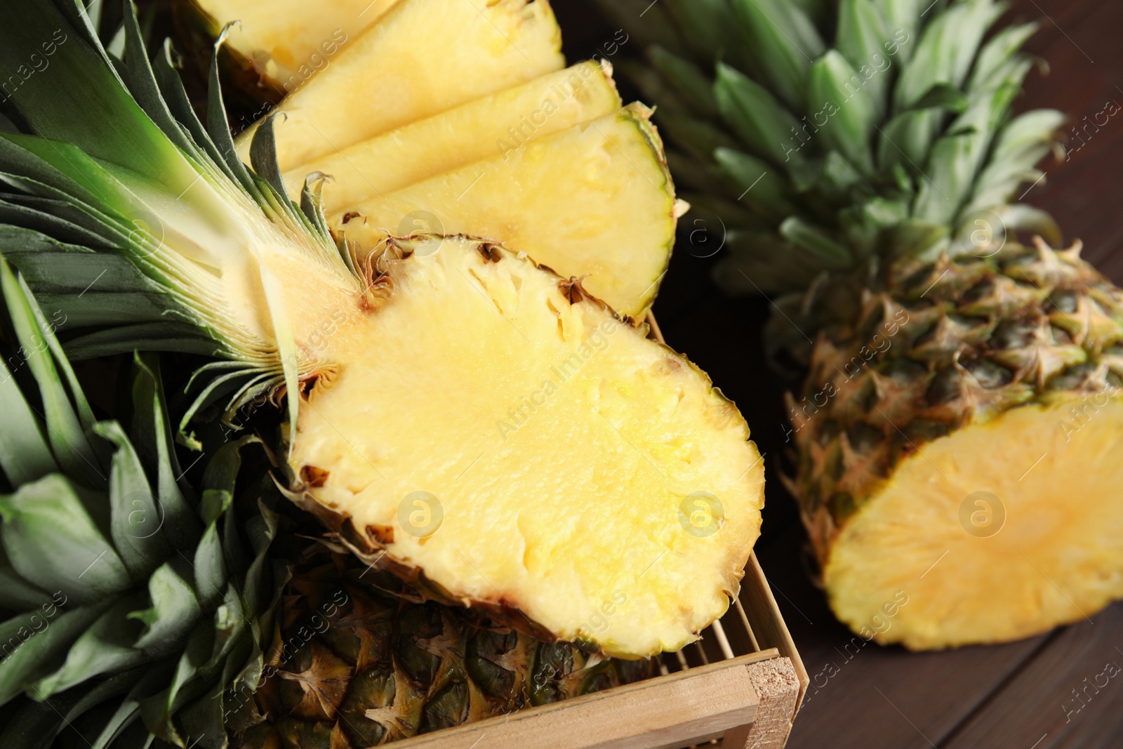 Photo of Tasty cut pineapples in wooden crate on table, closeup