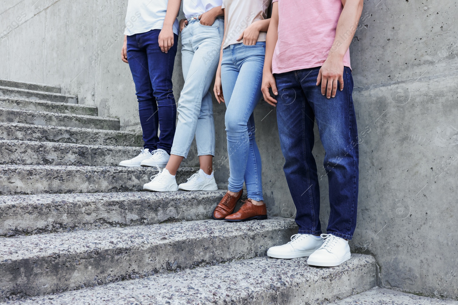 Photo of Group of people in stylish jeans on stairs near stone wall outdoors, closeup