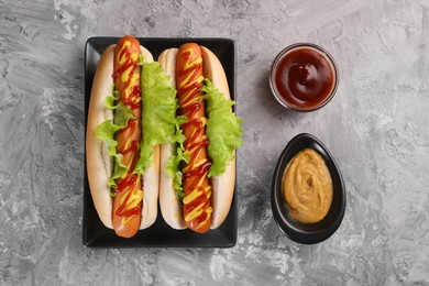 Photo of Tasty hot dogs with lettuce, ketchup and mustard on grey textured table, flat lay