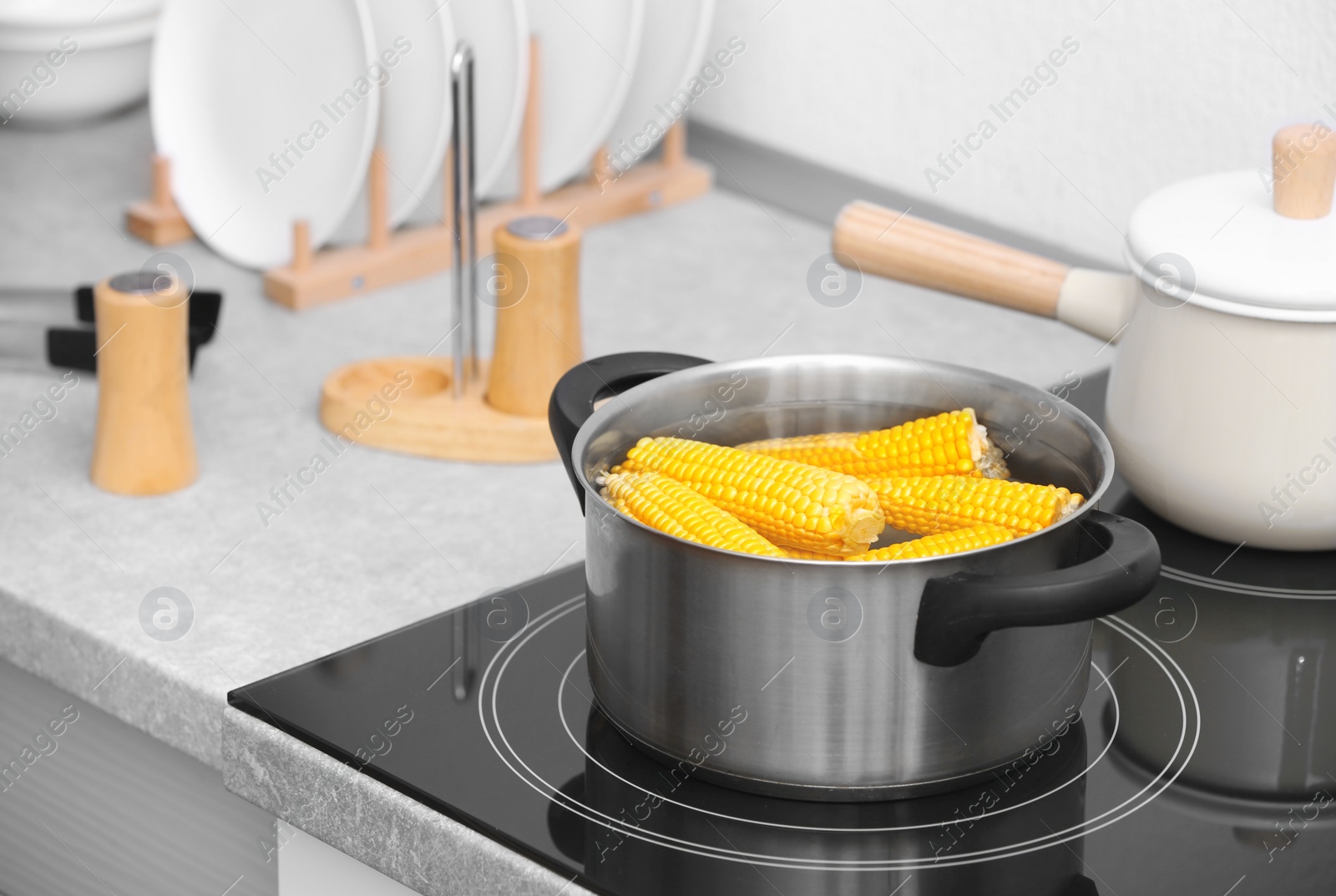 Photo of Stewpot with water and corn cobs on stove in kitchen