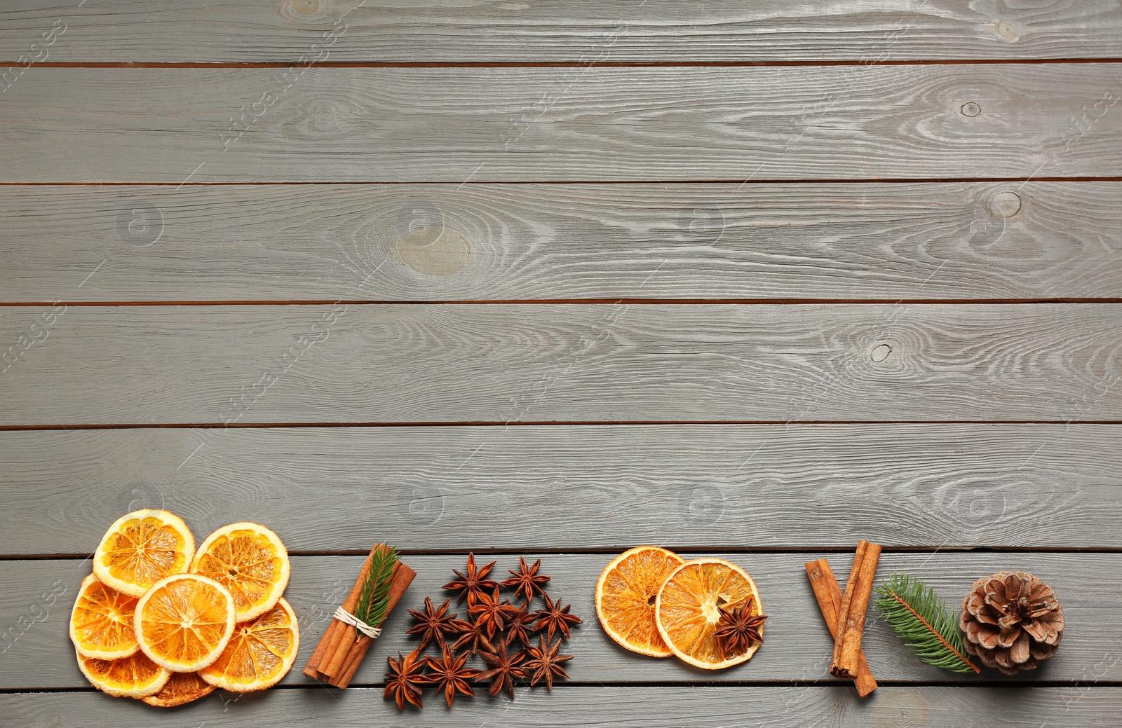 Photo of Flat lay composition with dry orange slices, anise stars and cinnamon sticks on grey wooden table. Space for text