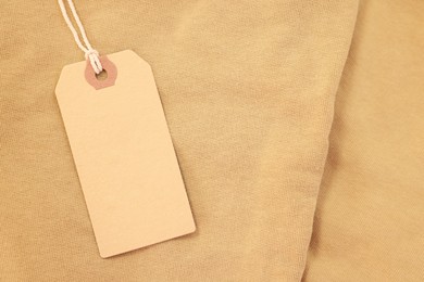 Photo of Cardboard tag on beige garment, top view. Space for text