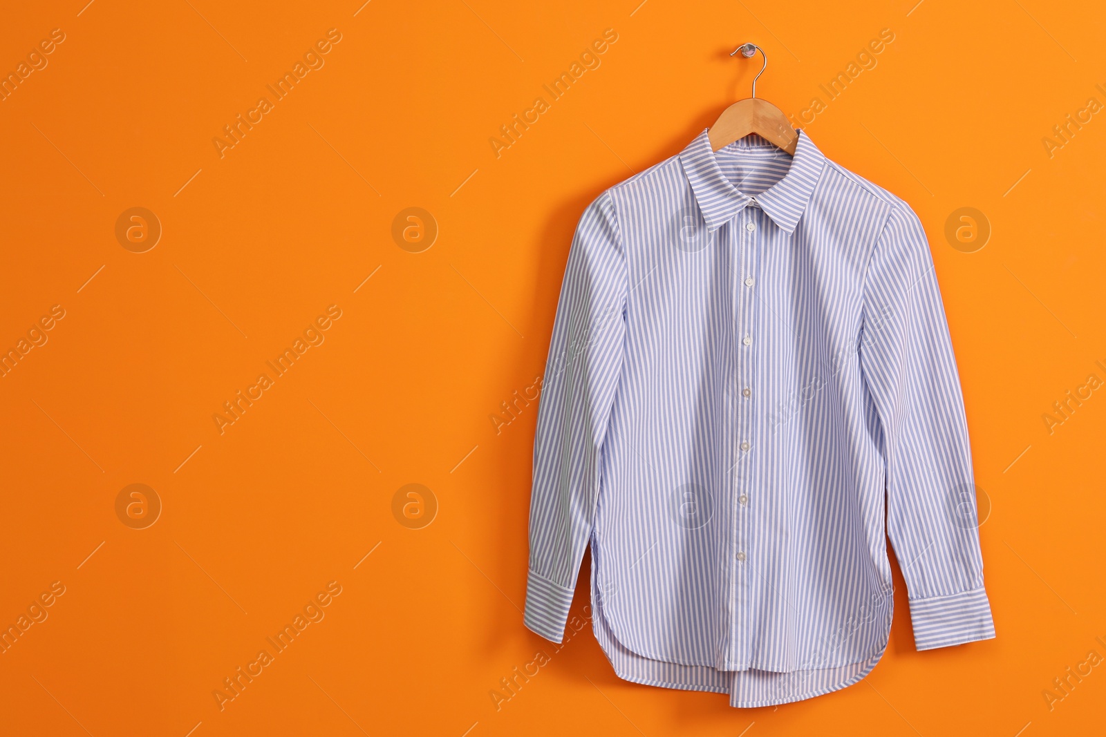 Photo of Hanger with striped shirt on orange wall, space for text