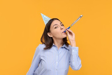 Young woman in party hat with blower on yellow background