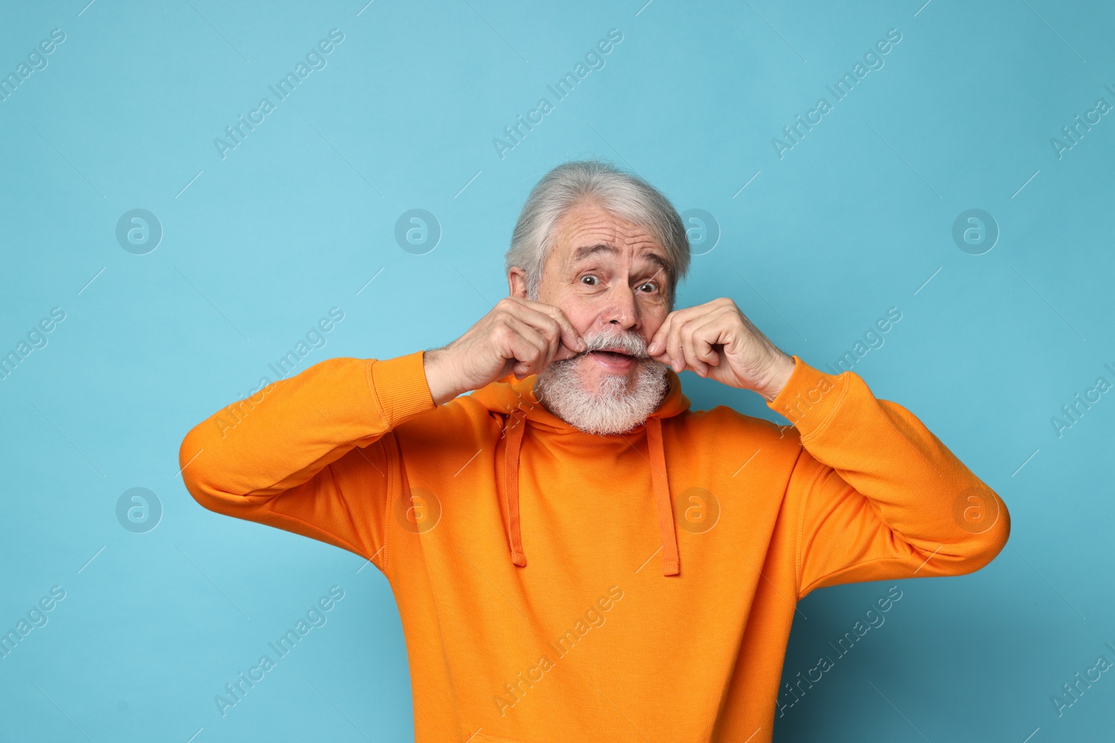 Photo of Senior man touching mustache on light blue background