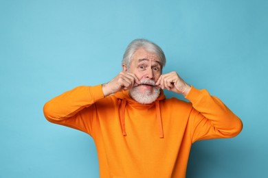 Senior man touching mustache on light blue background