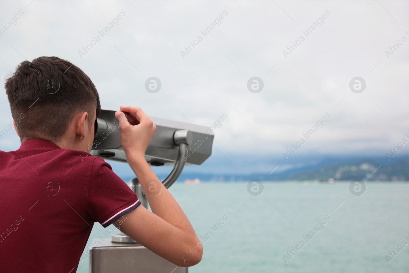 Photo of Teenage boy looking through mounted binoculars at mountains. Space for text