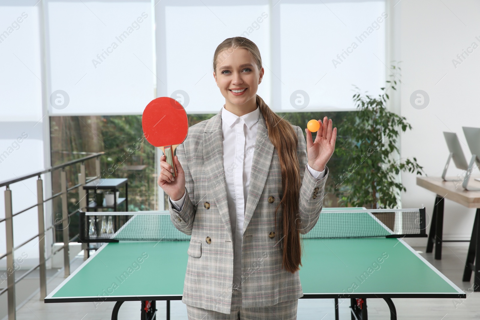 Photo of Business woman with tennis racket and ball near ping pong table in office