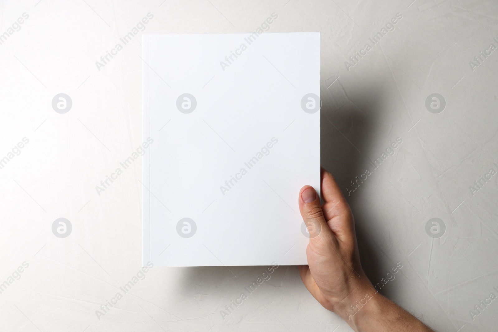 Photo of Man holding blank notebook at white table, top view. Mockup for design