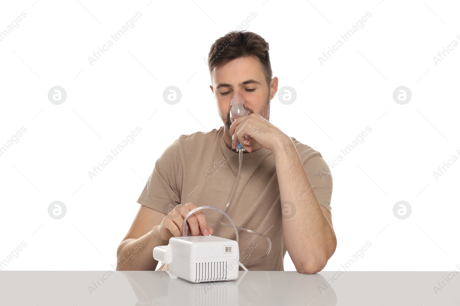 Photo of Sick man using nebulizer for inhalation at table on white background