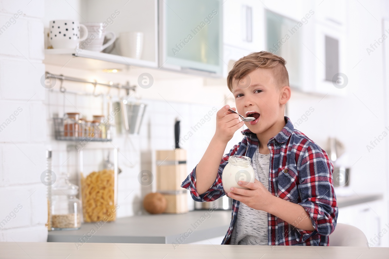 Photo of Little boy with yogurt in kitchen