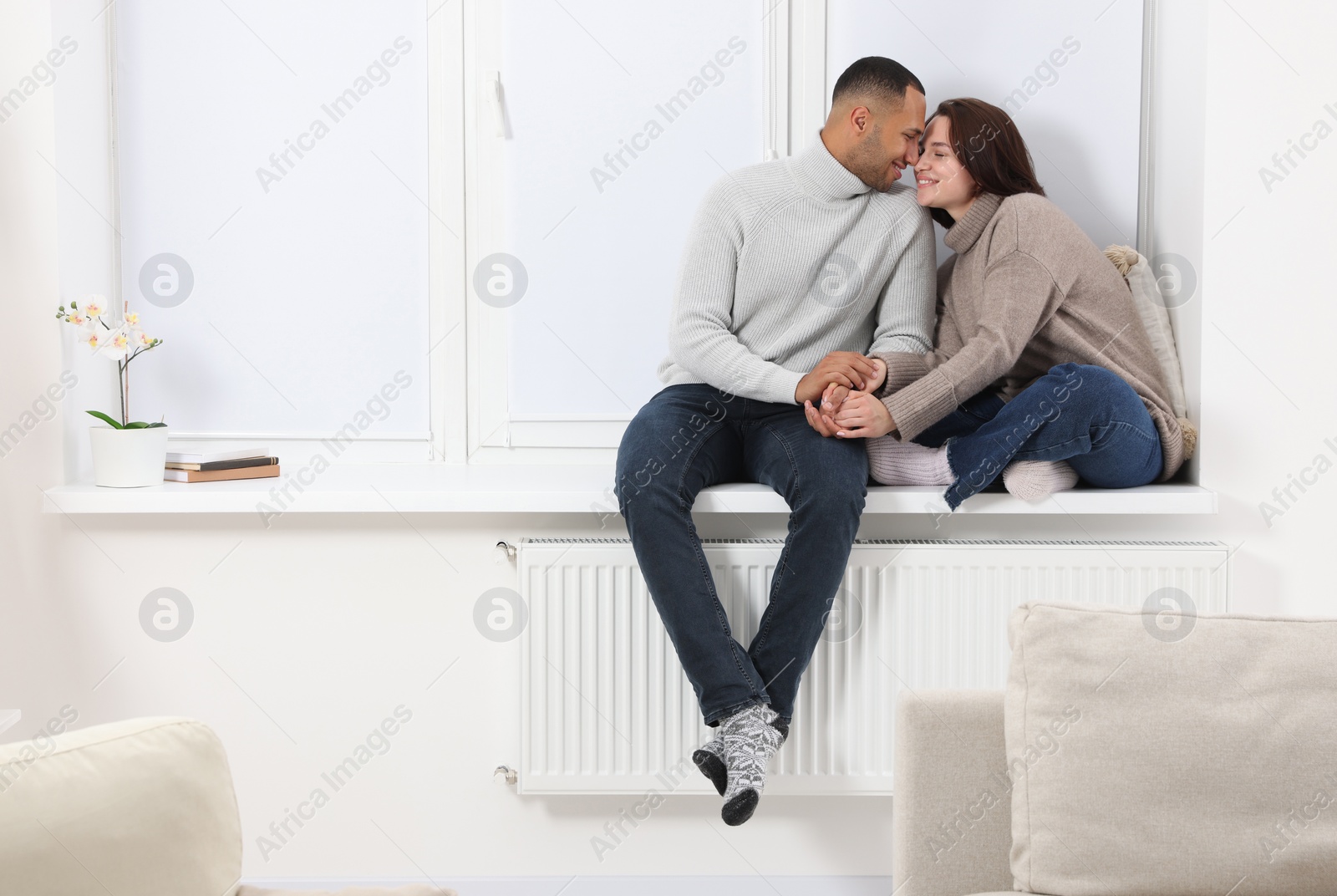 Photo of Dating agency. Happy couple holding hands and sitting on window sill at home, space for text