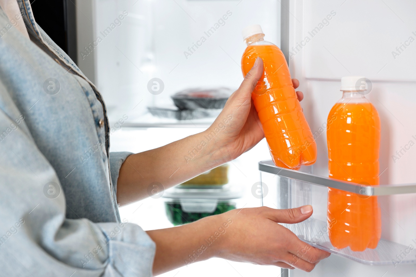 Photo of Young woman taking bottle of juice out of refrigerator, closeup
