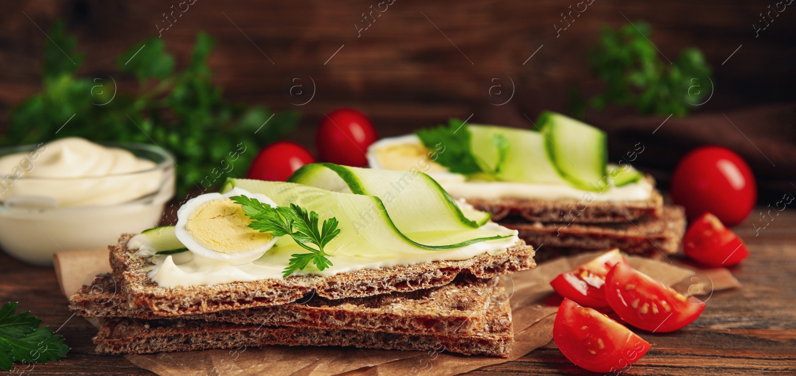 Photo of Fresh rye crispbreads with quail egg, cream cheese and cucumber slices on wooden table