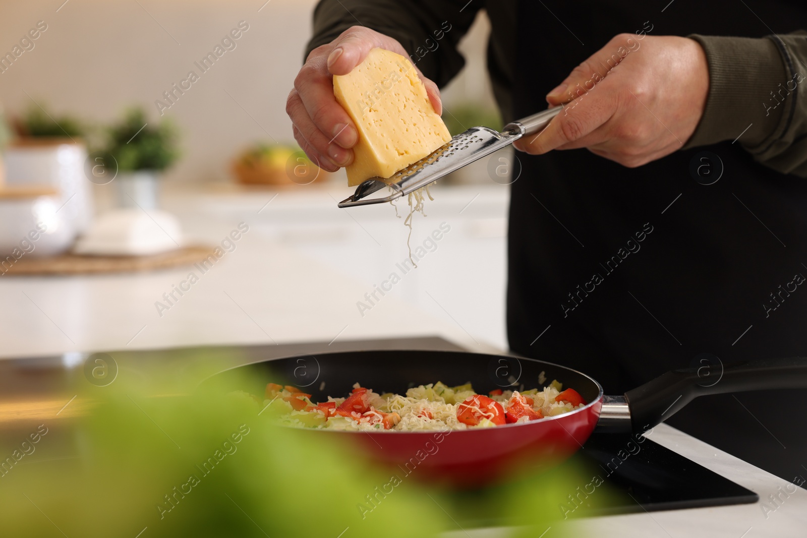 Photo of Cooking process. Man grating cheese into frying pan in kitchen, closeup