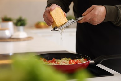 Cooking process. Man grating cheese into frying pan in kitchen, closeup