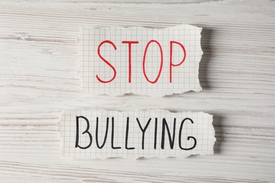 Photo of Scraps of paper with text Stop Bullying on white wooden table, flat lay