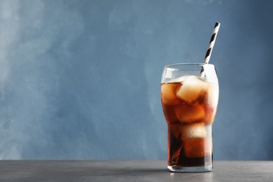 Glass of refreshing cola with ice on table against color background. Space for text