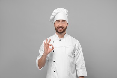 Smiling mature chef showing ok gesture on grey background